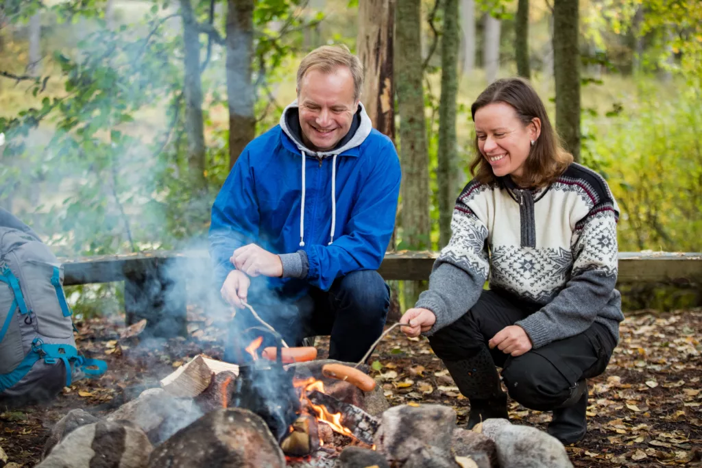 Man and woman roasting on campfire in forest on shore of lake