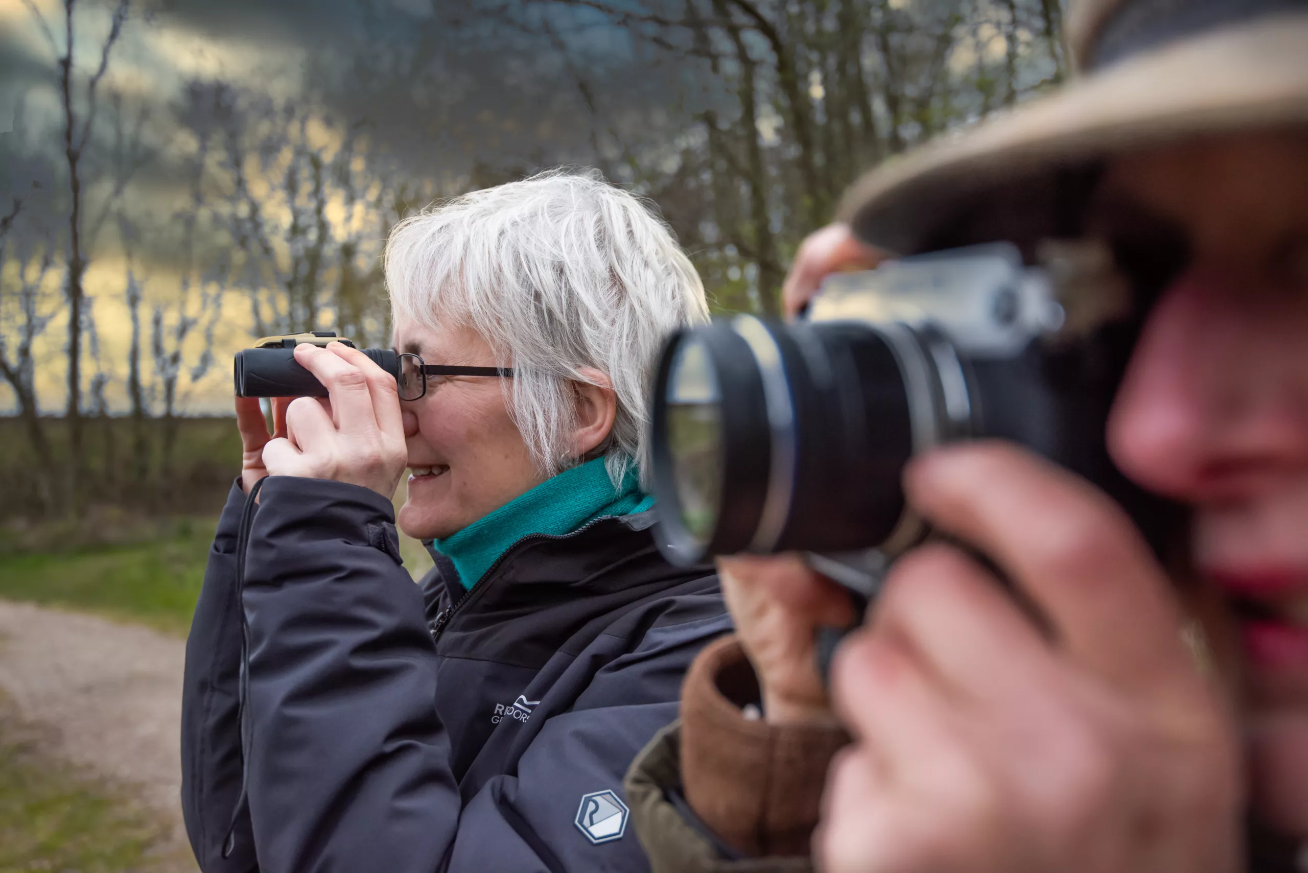 Woman looking through binoculars and man taking a photo at Kelling Heath