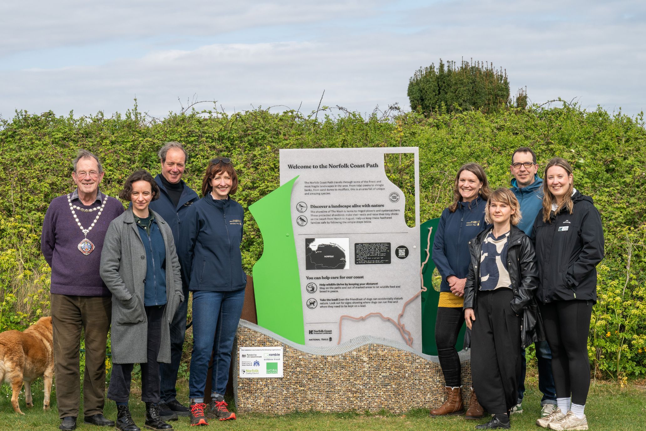 A group photo of people beside the new interpretation board, there are four people to the left of the board and four people to the right. The people from left to right are Cllr Michael Ruston - Chairman of Council & Mayor of Hunstanton, Chloe France - Senior Manager: National Trails and Open Access, Cllr Andrew Jamieson - Chair of the Norfolk National Trail Partnership, Dr Katy Owen - Protected Landscapes Manager at Norfolk County Council, Helen Terry – National Trial Team Leader, Sam Williams – Designer of Interpretation Boards, Alex Stewart - Digital Marketing Manager Ramble Worldwide, Zoë Carruthers – Engagement and Branding Officer, Norfolk Coast Protected Landscapes.