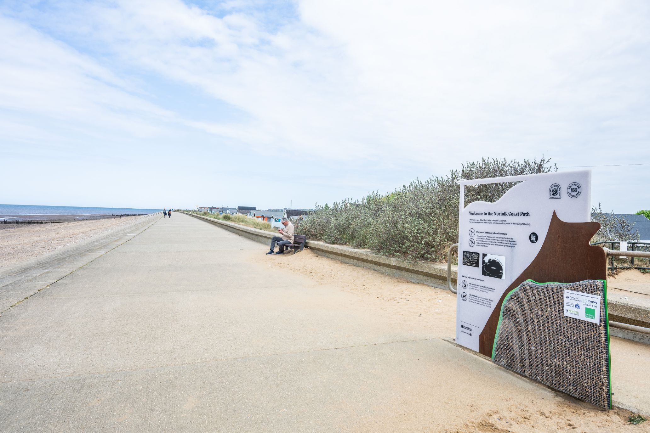 A wide landscape shot of the walkway beside the beach with one of the new interpretation panels to the very right of the image.